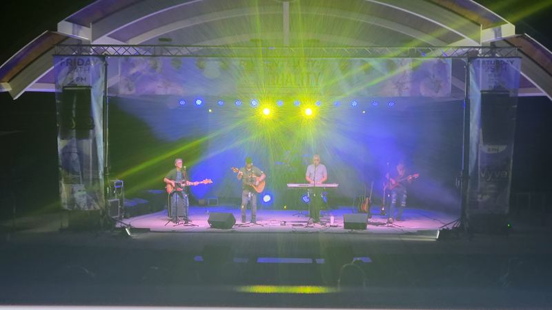 Band on an amphitheater stage under green and blue beams