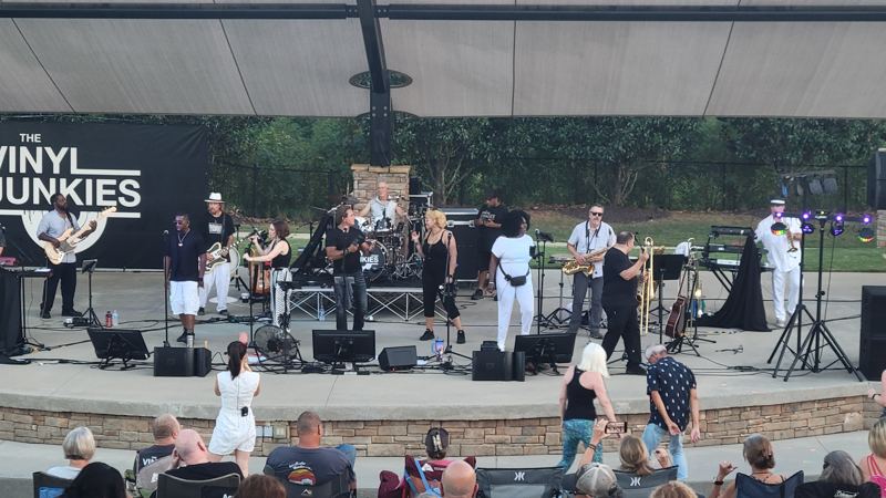Large band performing on an outdoor stage for a seated crowd